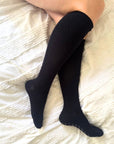 pregnant women wearing navy compression knee-high socks on a white textured surface